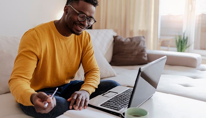 Smiling Man in Orange Shirt Using Computer at Home