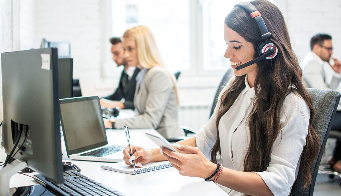 People Sitting a Desks and a Woman With Headphones Taking Notes