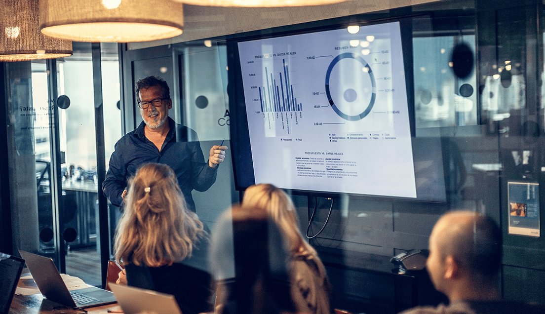 Man Presenting Graphs on a Smartboard in a Room Full of People
