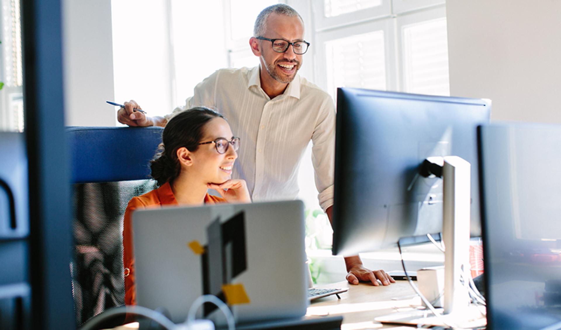 Two People in an Office Looking at a Computer and Smiling