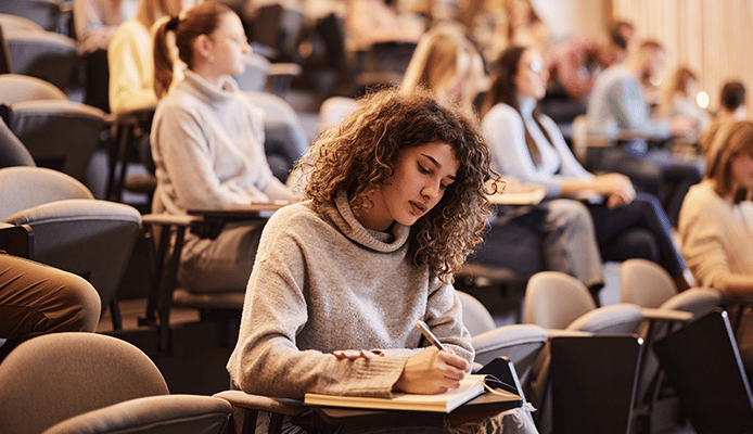 Woman With Curly Hair Writing Notes in Classroom Setting
