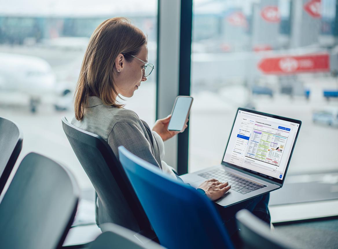 Woman Using Laptop and Phone in Airport Waiting Area