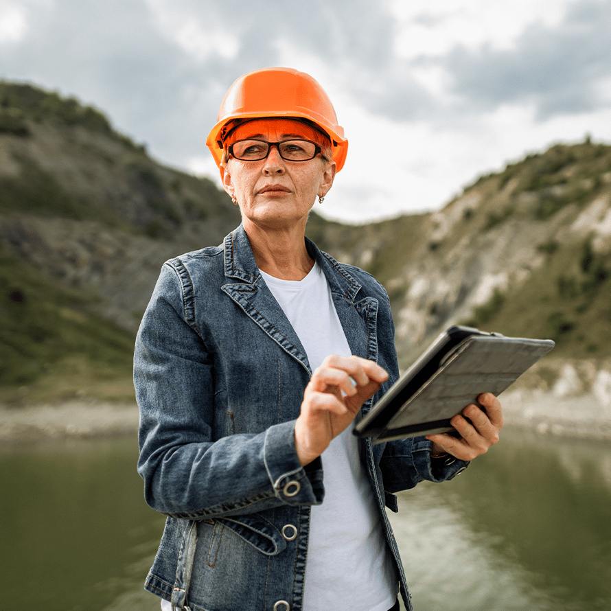 Woman Wearing Orange Hard Hat and Holding Tablet Out in Nature