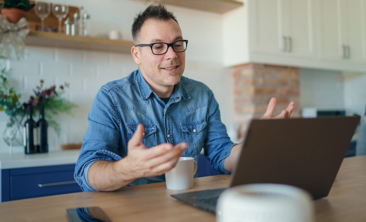 A cheerful man wearing glasses interacts with his laptop during a virtual lesson, representing the ease and accessibility of learning Danish online from home.