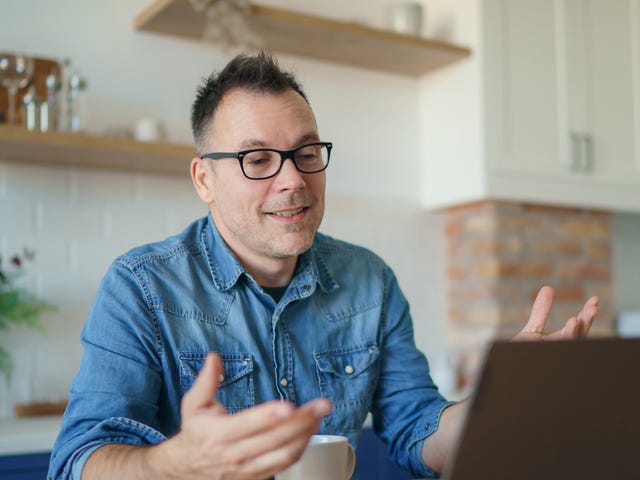 A cheerful man wearing glasses interacts with his laptop during a virtual lesson, representing the ease and accessibility of learning Danish online from home.