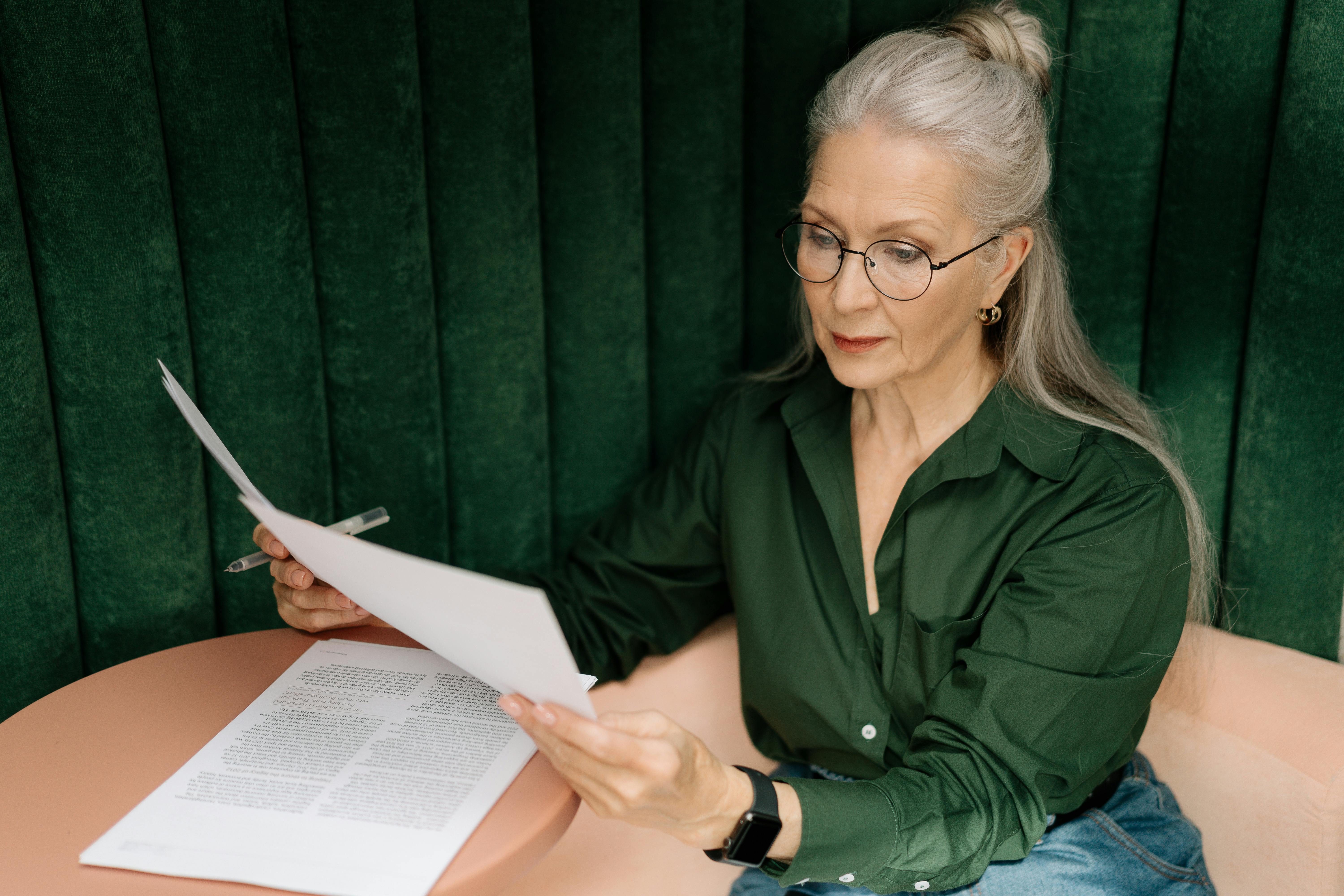 Elderly woman in glasses holding a piece of paper and checking examples for the present continuous tense in English