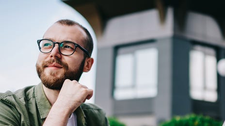 A young man in glasses sits outside with his laptop, smiling as he studies, representing Spanish vocabulary lessons through remote online learning.