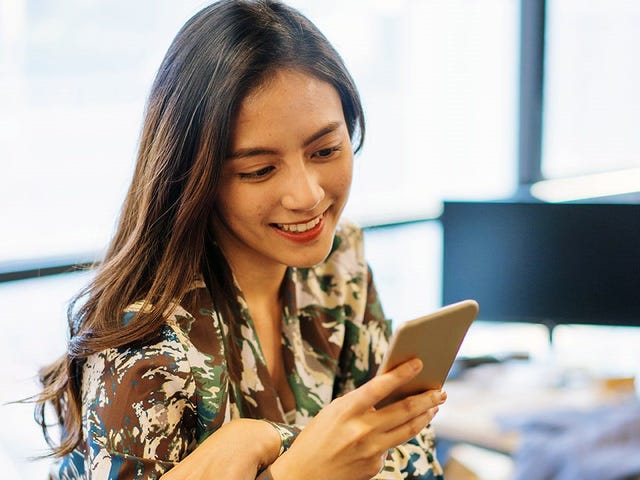 A woman in an office setting, smiling while using her phone, representing a modern approach to global corporate language training.