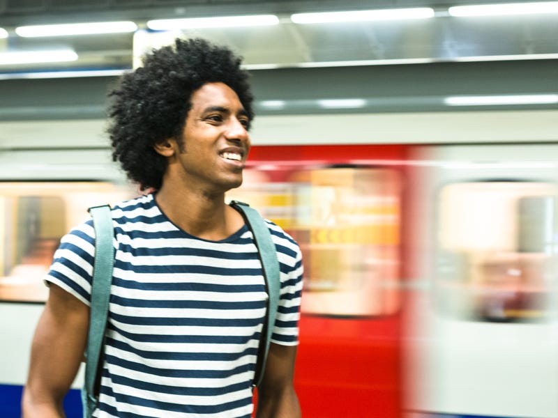 Young man waiting for a train while learning Portuguese online using a mobile device.
