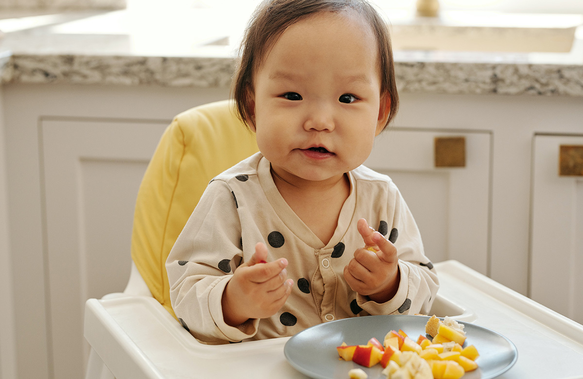 Baby eating fruit that has been cut up into small pieces.