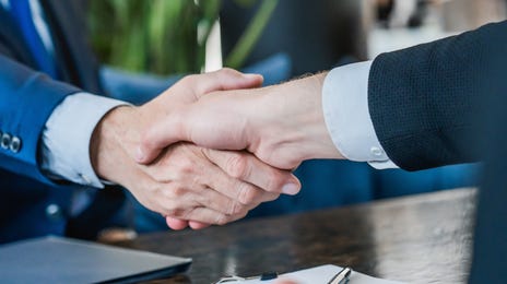 Two professionals in formal attire shaking hands at a business meeting, representing successful agreements and the importance of government translation services.