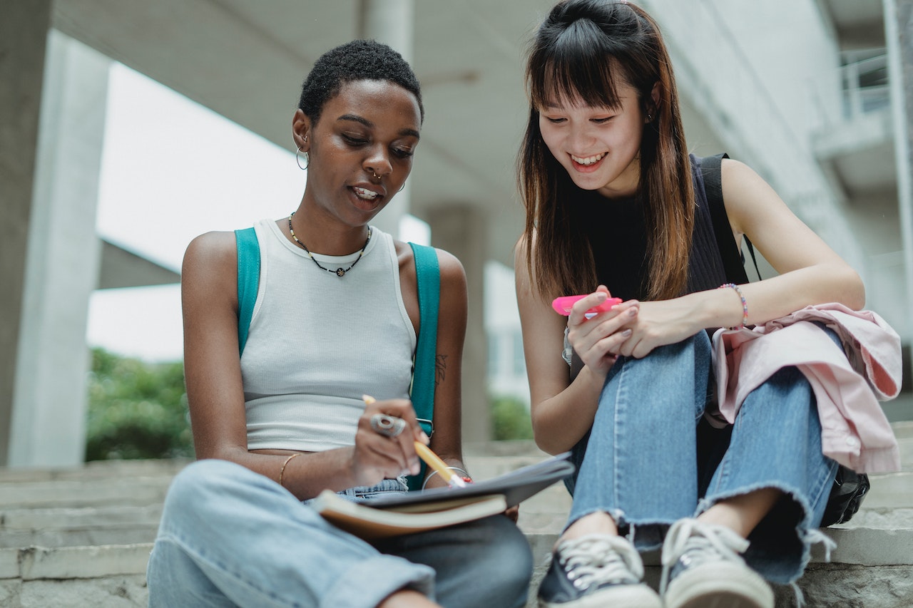 These two diverse happy female students are learning about English abbreviations, slang and acronyms.