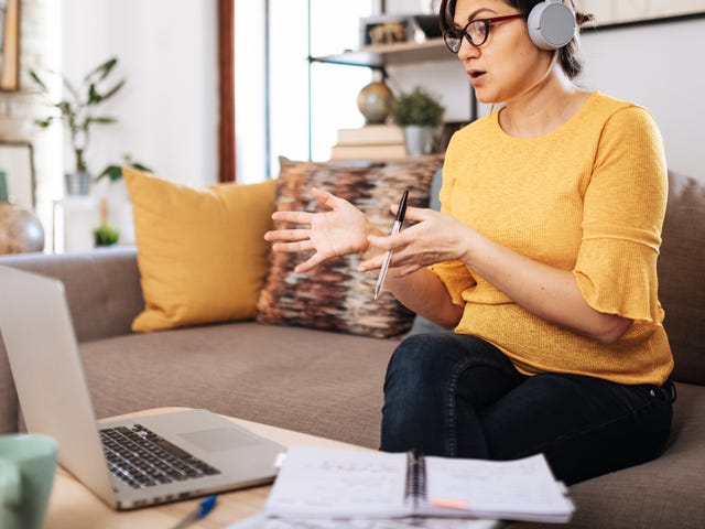 Woman learning Czech language online from home using a laptop, taking notes and wearing headphones