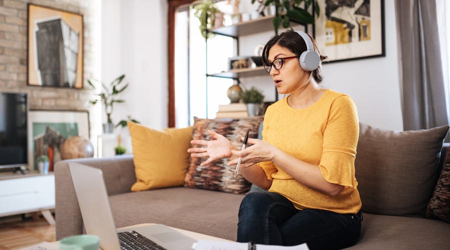 Woman learning Czech language online from home using a laptop, taking notes and wearing headphones