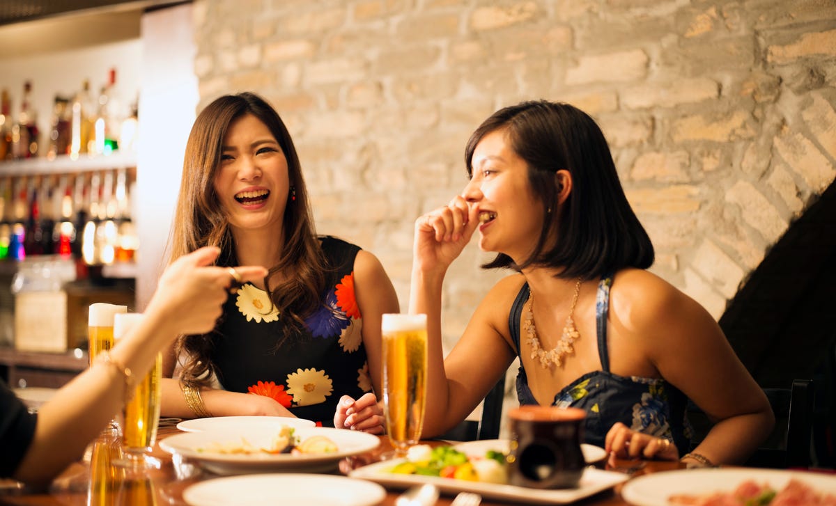 Two women laughing and conversing during advanced Spanish lessons at a cozy dinner setting.