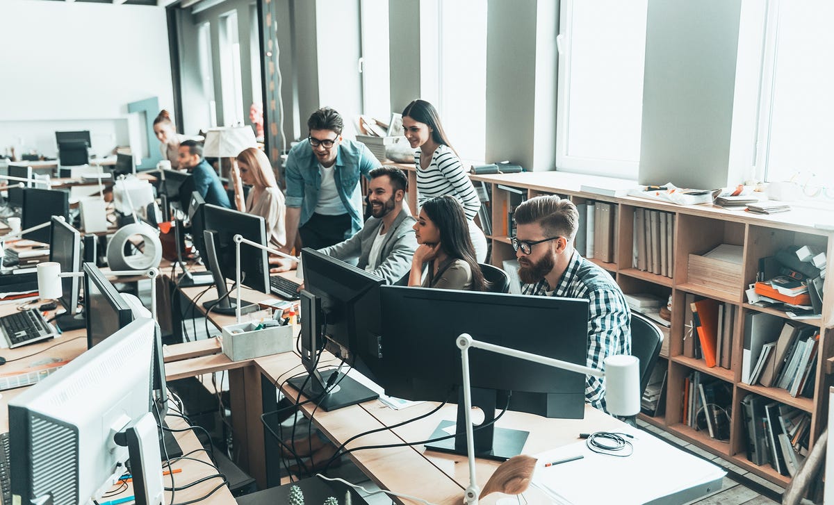 A group of professionals working and learning together in a modern open-plan office, symbolizing group Spanish classes in a dynamic setting.