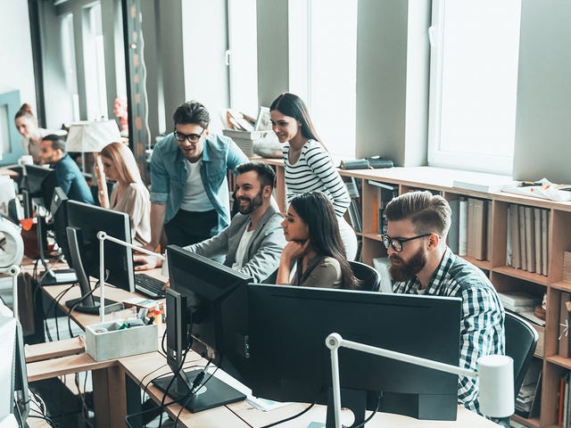 A group of professionals working and learning together in a modern open-plan office, symbolizing group Spanish classes in a dynamic setting.