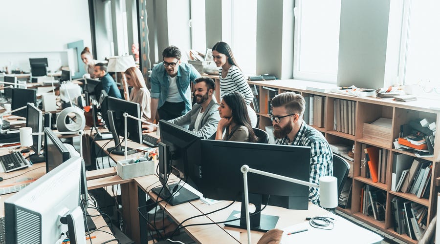 A group of professionals working and learning together in a modern open-plan office, symbolizing group Spanish classes in a dynamic setting.
