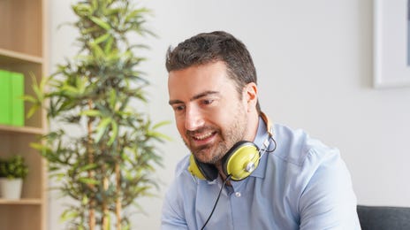 Man learning intermediate Spanish online at home with headphones and a laptop, enjoying a relaxed study environment