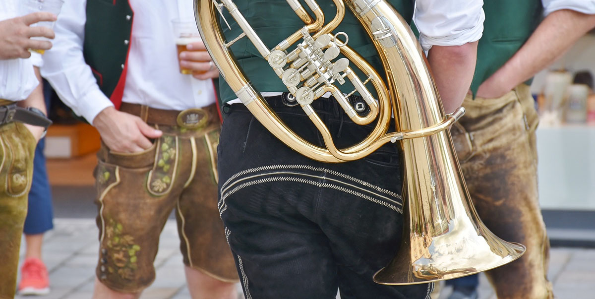 People in Lederhosen and Dirndl dresses, chugging beer from jugs while brass music is playing in the background.