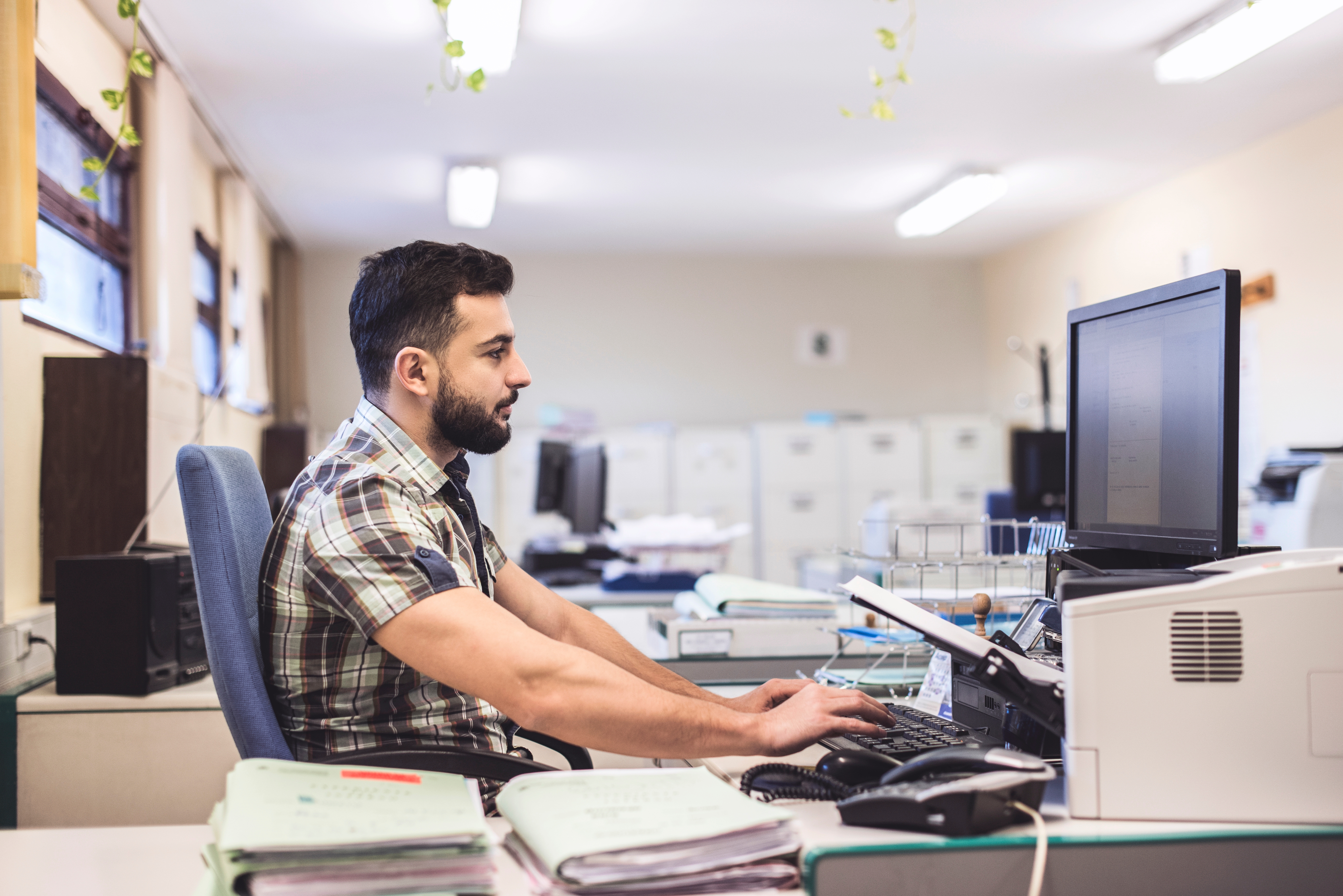 Man taking a written English test on a desktop computer in a quiet office setting, focused on typing.

