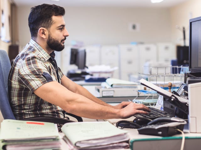 Man taking a written English test on a desktop computer in a quiet office setting, focused on typing.