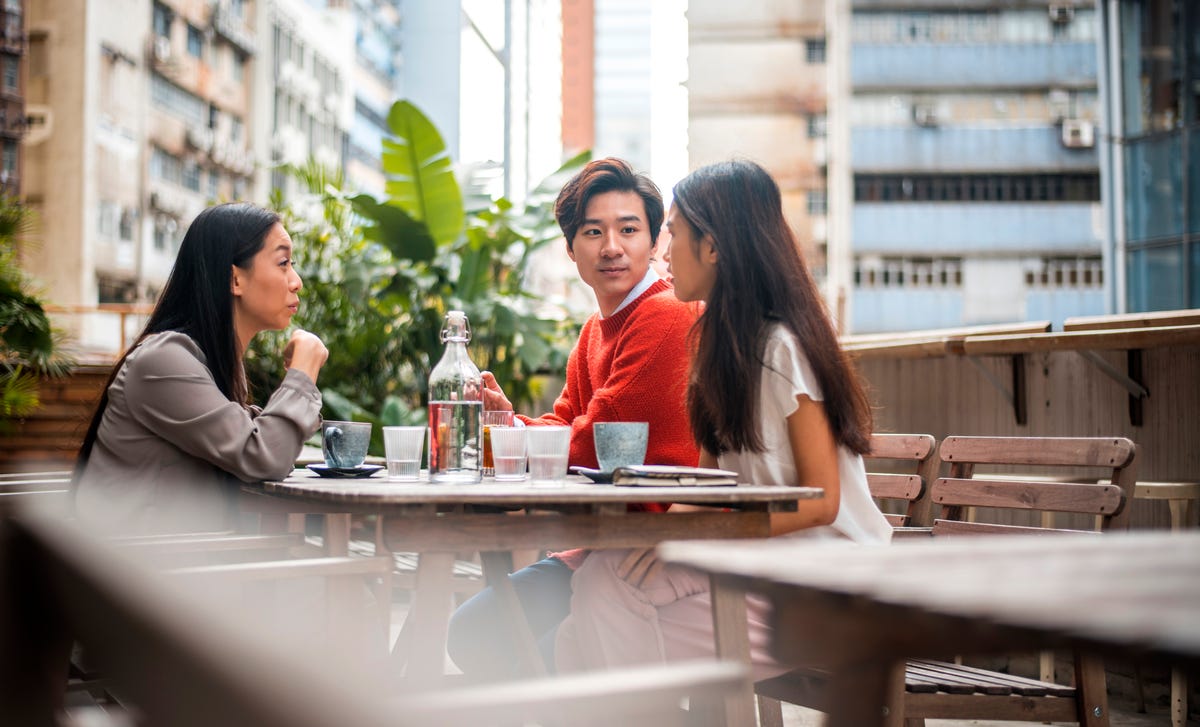 Three young adults having a casual Cantonese conversation at an outdoor cafe in the city