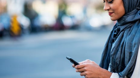 A woman in a hijab using a smartphone on a city street, symbolizing the modern and flexible way to learn Hindi online anytime, anywhere.