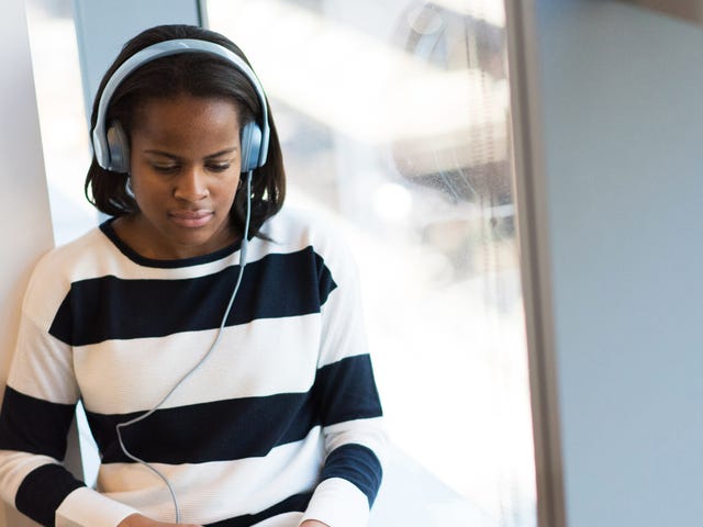 Focused young woman wearing headphones and studying on her laptop during an online Korean class by the window.