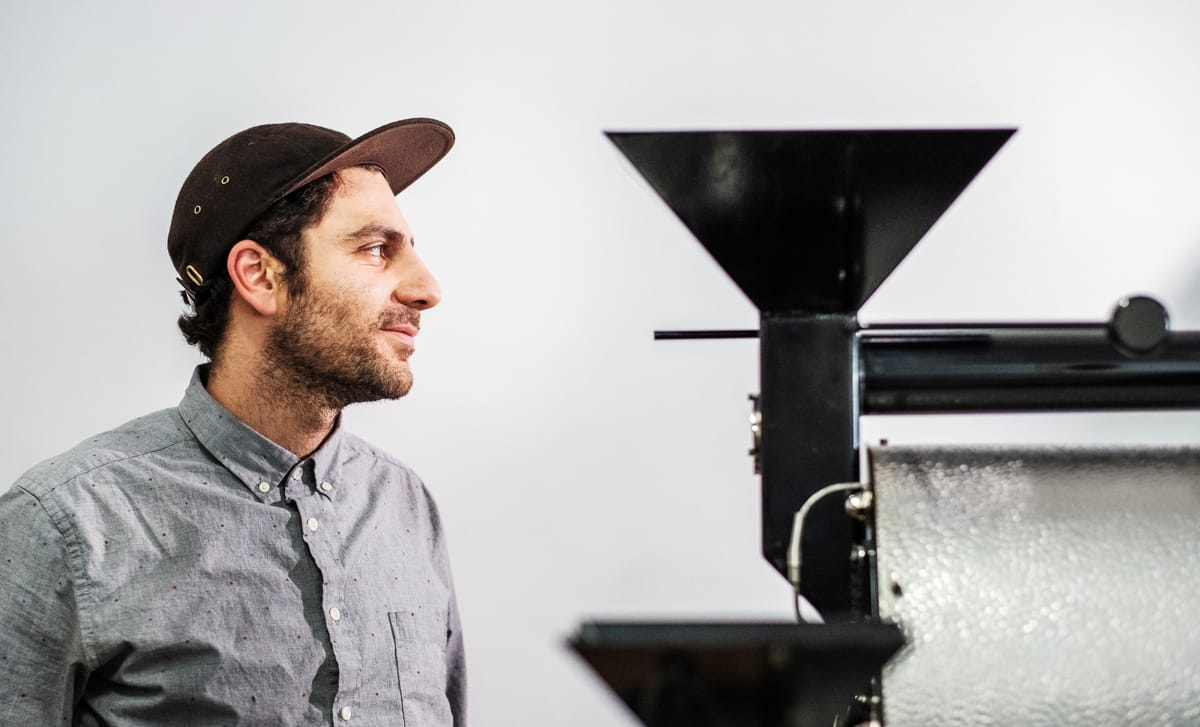 A man in a casual cap and button-down shirt working near industrial machinery, representing practical, hands-on ways to learn advanced German in a professional setting.