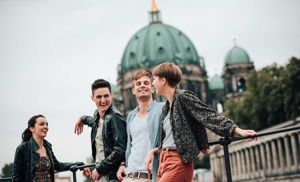 Group of young adults smiling and chatting outside a historic building in Berlin, symbolizing the cultural immersion offered by Berlitz language school programs.