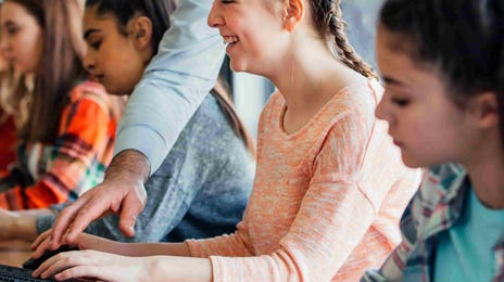 Teacher helping students in a computer classroom.