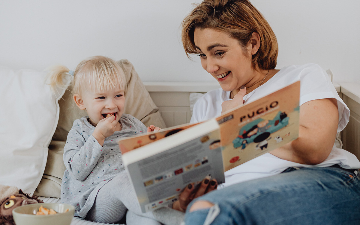 Mother reading her daughter a book full of funny Spanish words.