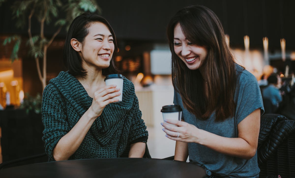 Two women smiling and practicing Norwegian conversation over coffee