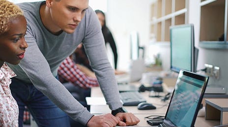 Team collaborating around a laptop in a modern workspace, highlighting Berlitz training tools that support professionals who teach Spanish online.