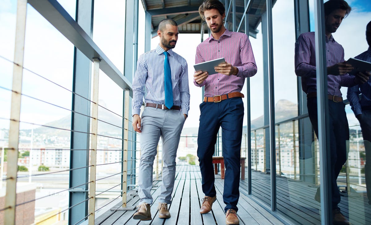 Two business professionals walking and discussing content on a tablet, symbolizing flexible private language lessons in a corporate setting.