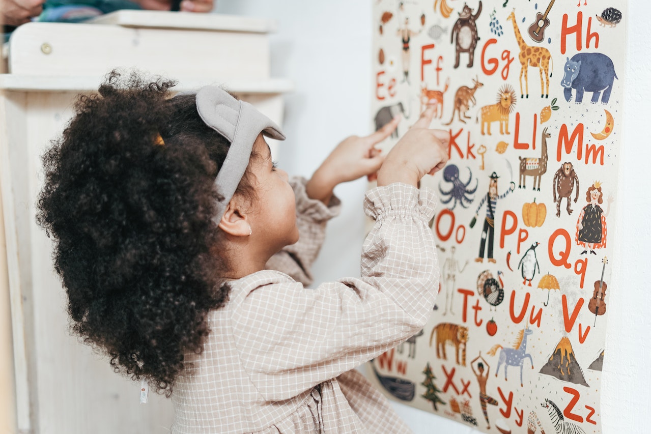 Young girl is learning French vowels and sounds with an alphabet poster with cartoon animals.