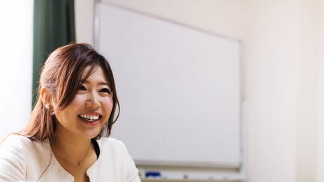 A woman in a business setting smiling and holding a document, representing a professional and engaging way to learn Indonesian online.