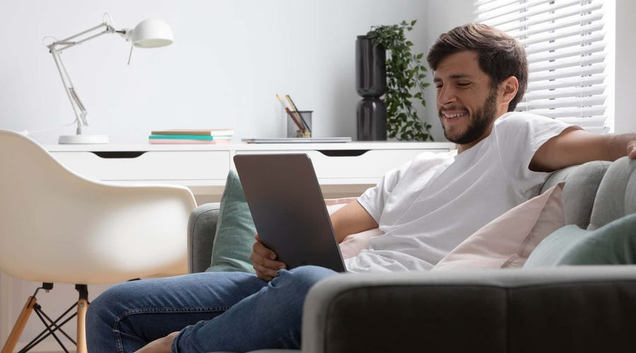 Man relaxing on a couch while using a tablet at home.