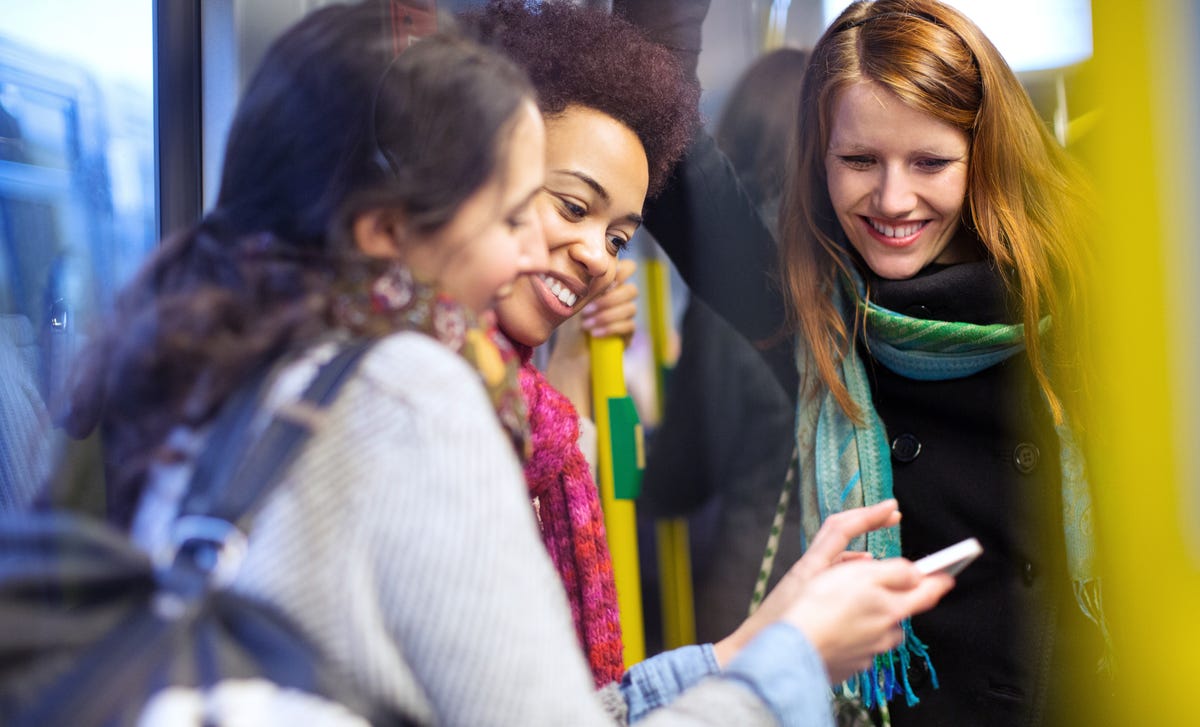Group of young women smiling and looking at a phone while riding public transport