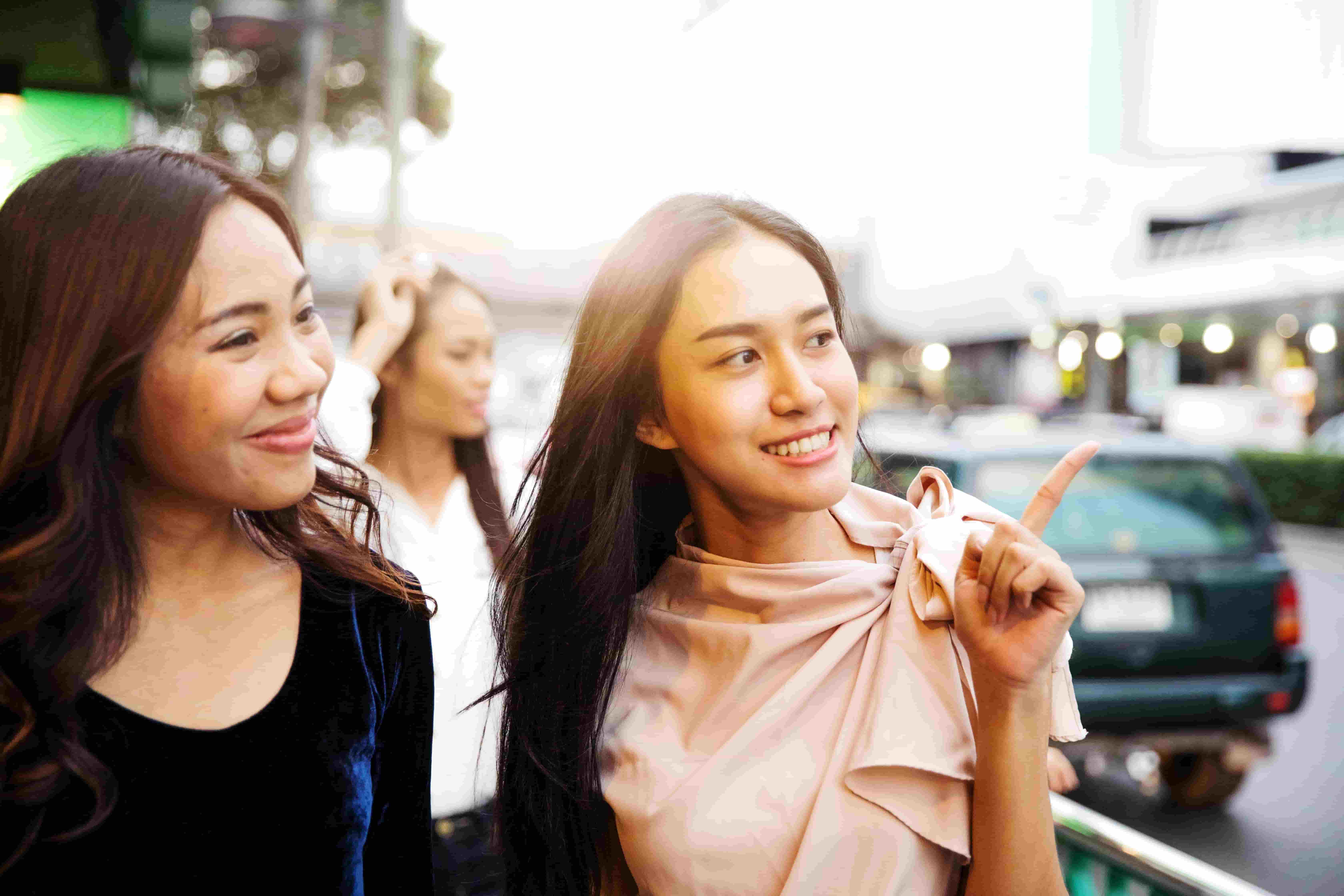 Two young women smiling while pointing and talking, symbolizing confidence gained from a Berlitz English speaking course.

