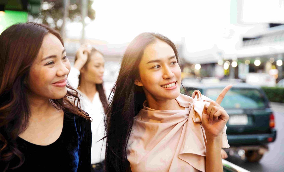Two young women smiling while pointing and talking, symbolizing confidence gained from a Berlitz English speaking course.