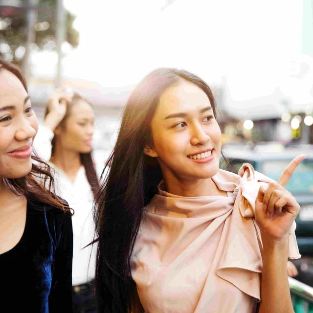 Two young women smiling while pointing and talking, symbolizing confidence gained from a Berlitz English speaking course.