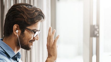 A man joins a video call from home, smiling and waving at his laptop.