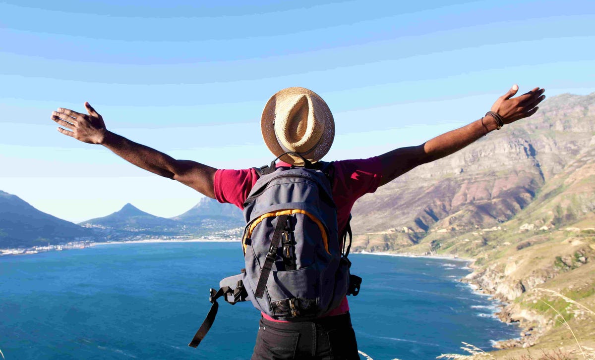 Man with backpack embracing a scenic ocean view from a mountaintop.