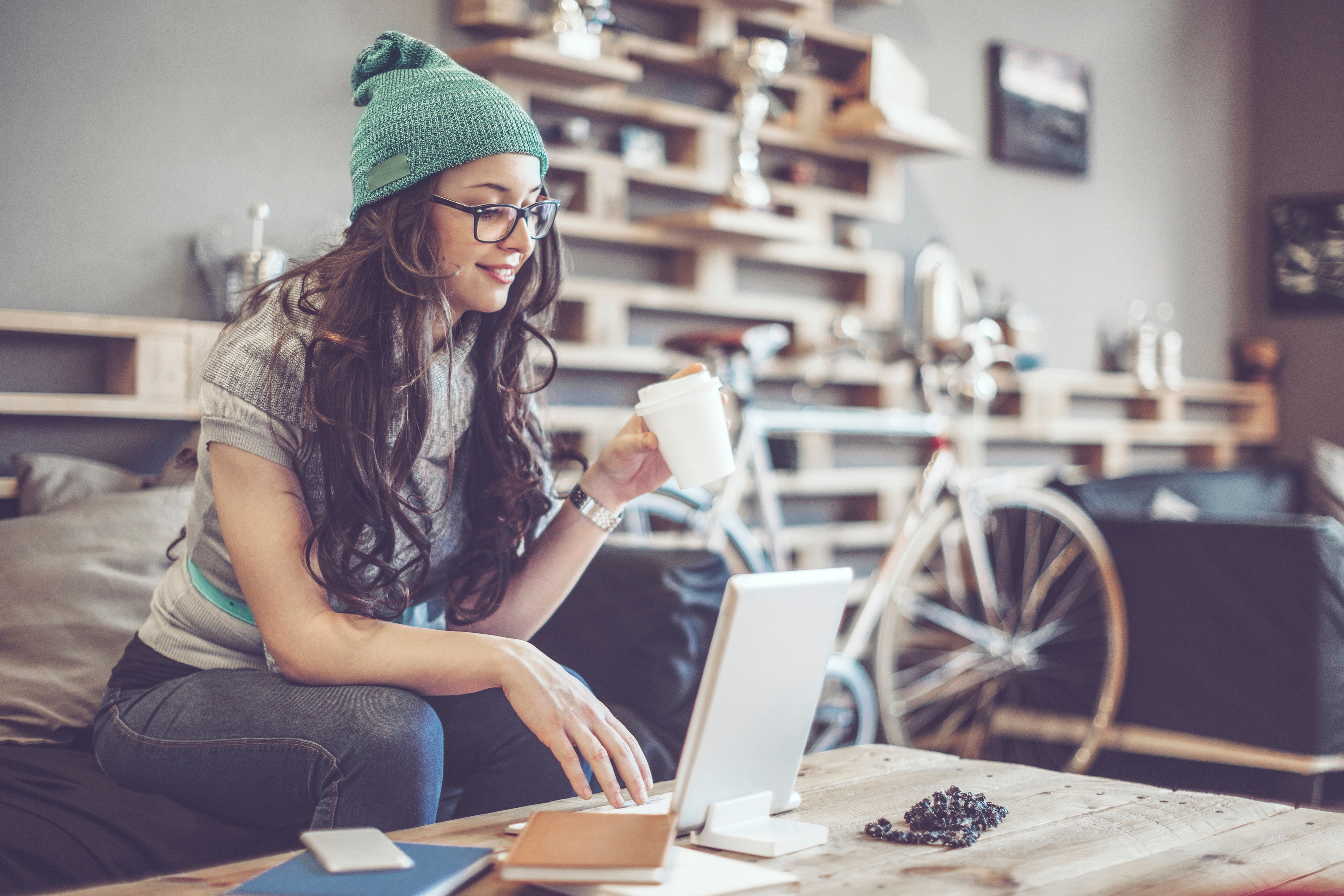 Young woman wearing glasses and a beanie learning Croatian online with a laptop and coffee at home

