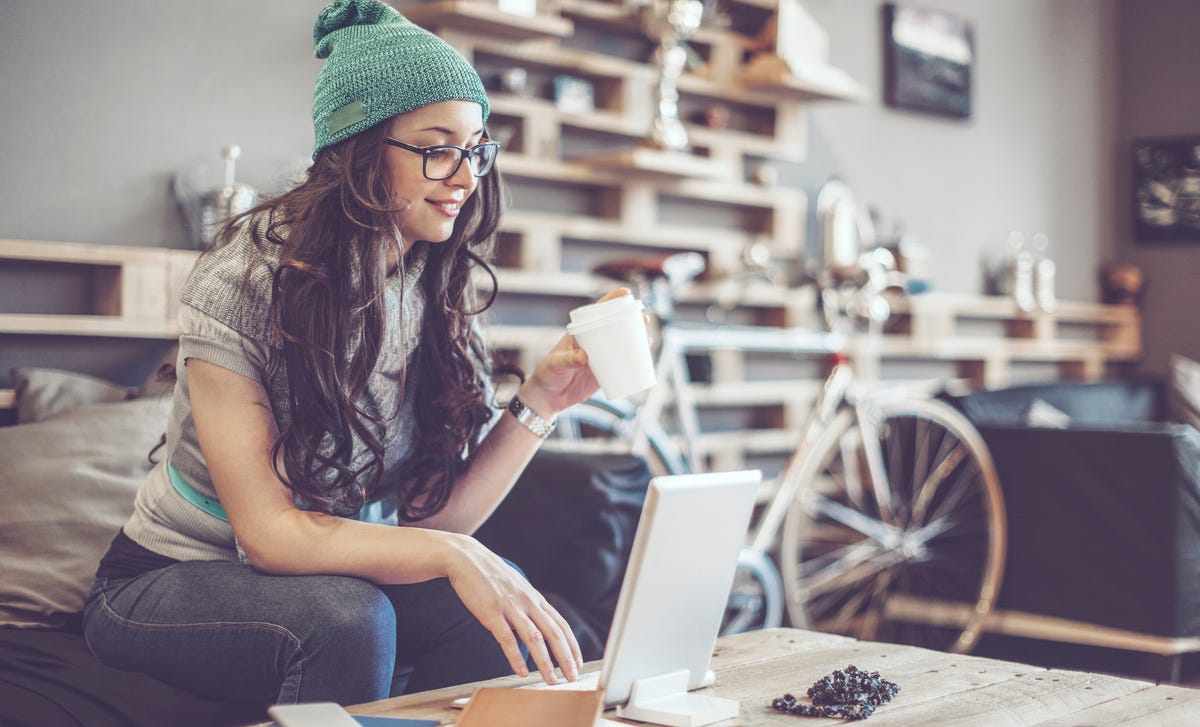 Young woman wearing glasses and a beanie learning Croatian online with a laptop and coffee at home
