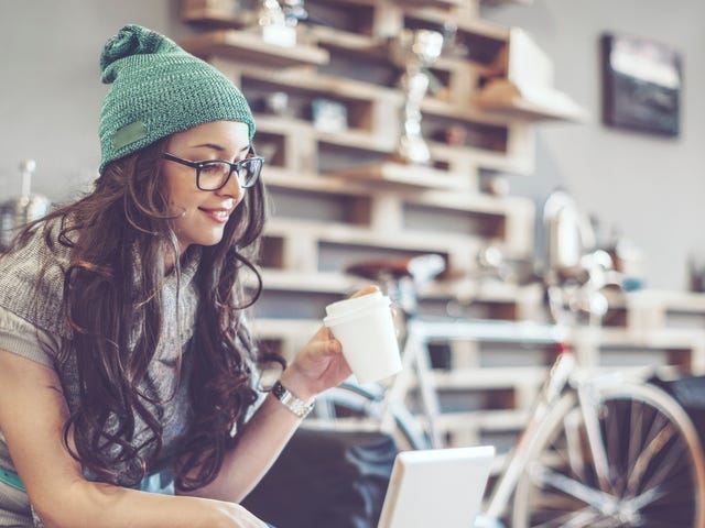 Young woman wearing glasses and a beanie learning Croatian online with a laptop and coffee at home