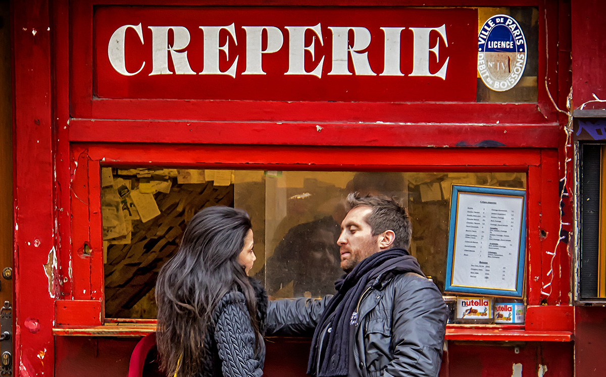 Couple standing in front of a Crêperie to order food in French.