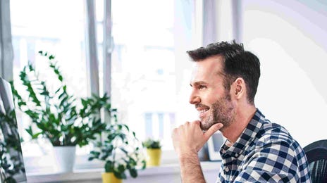 Smiling man working remotely at a desk with a computer, ideal for flexible German tutor jobs online.